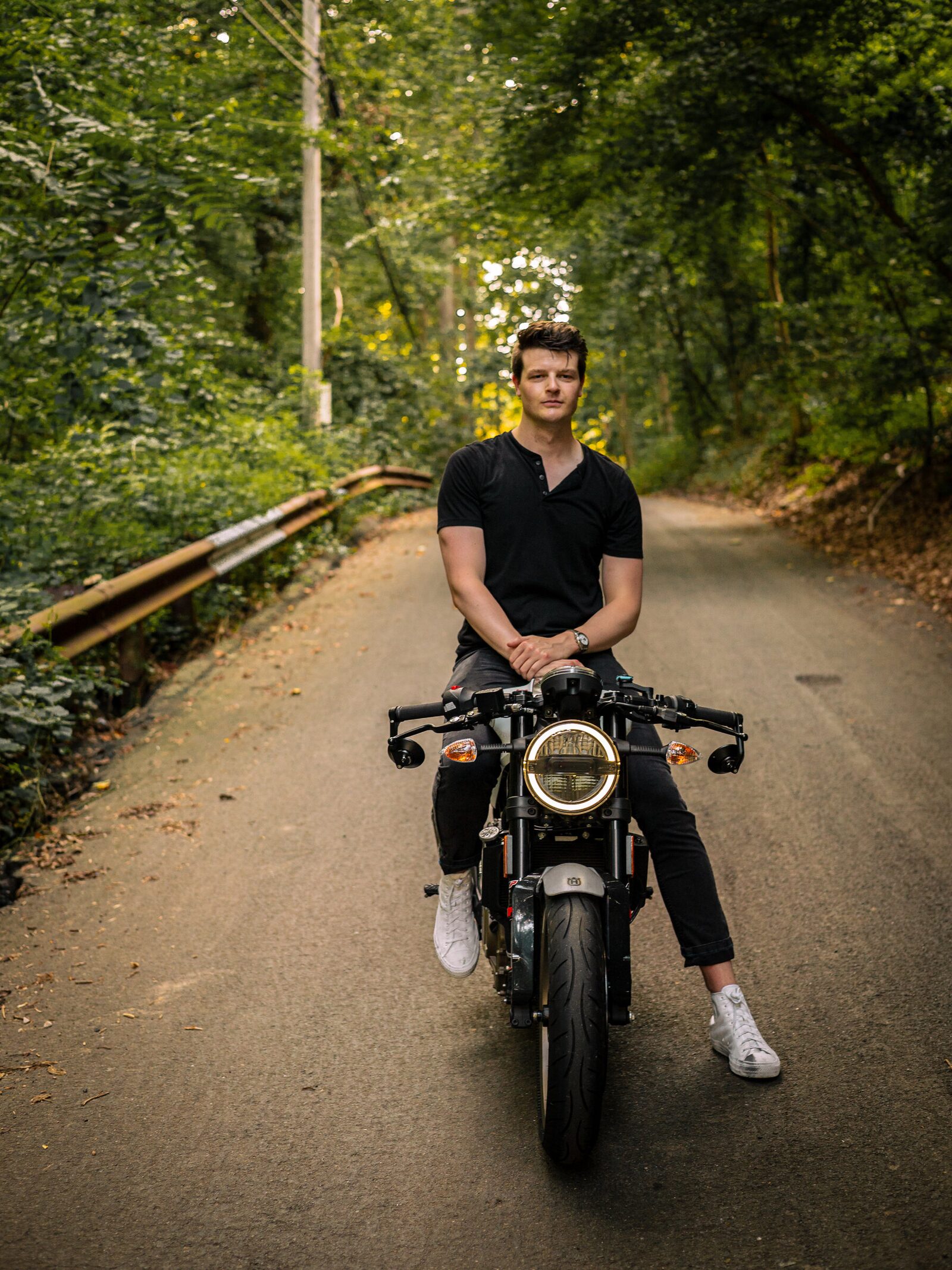Portrait photographer Keegan Duerr seated on a motorcycle on a wooded road