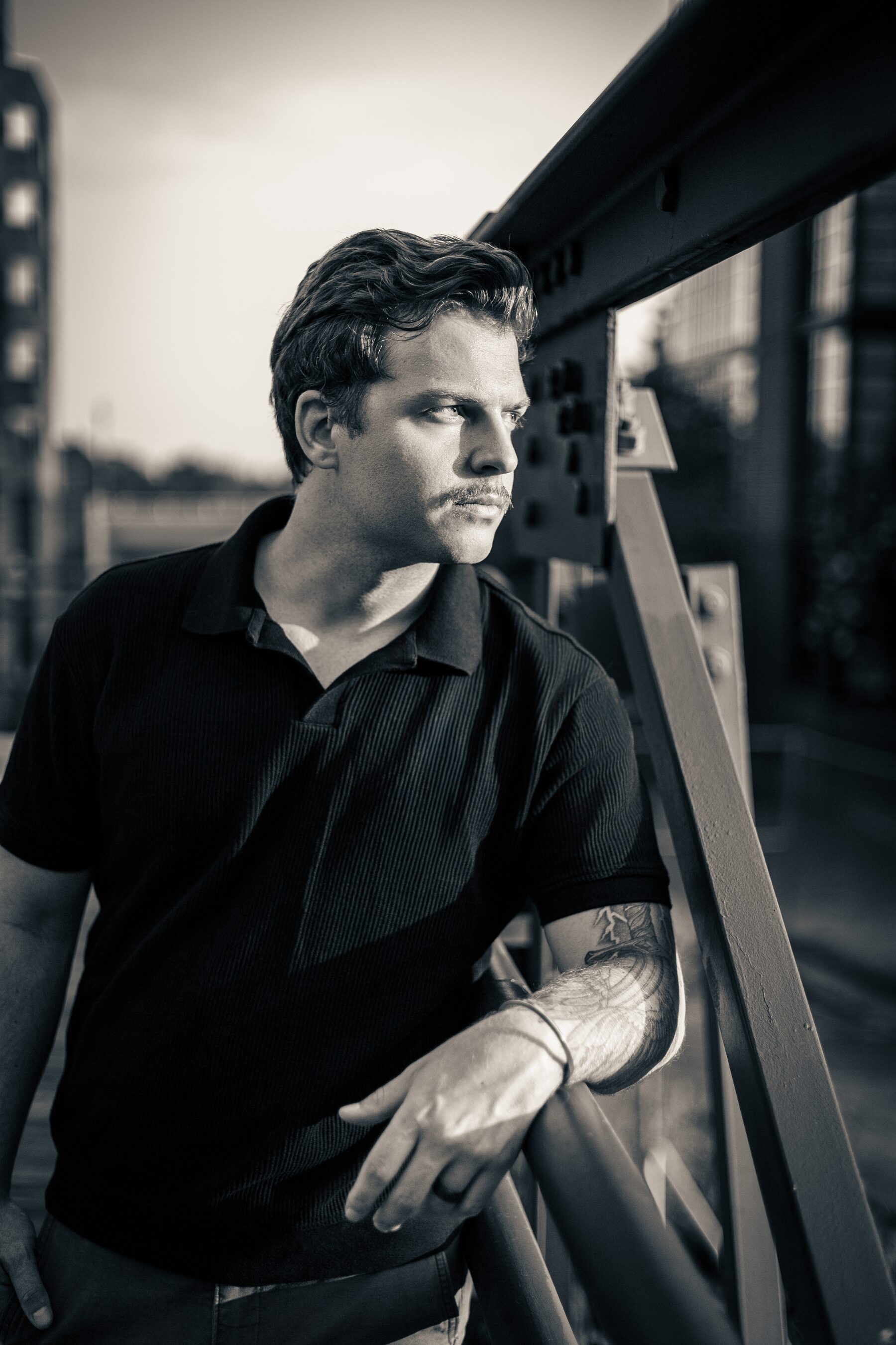 Black-and-white editorial portrait of a man leaning against a waterfront railing in Washington, D.C.