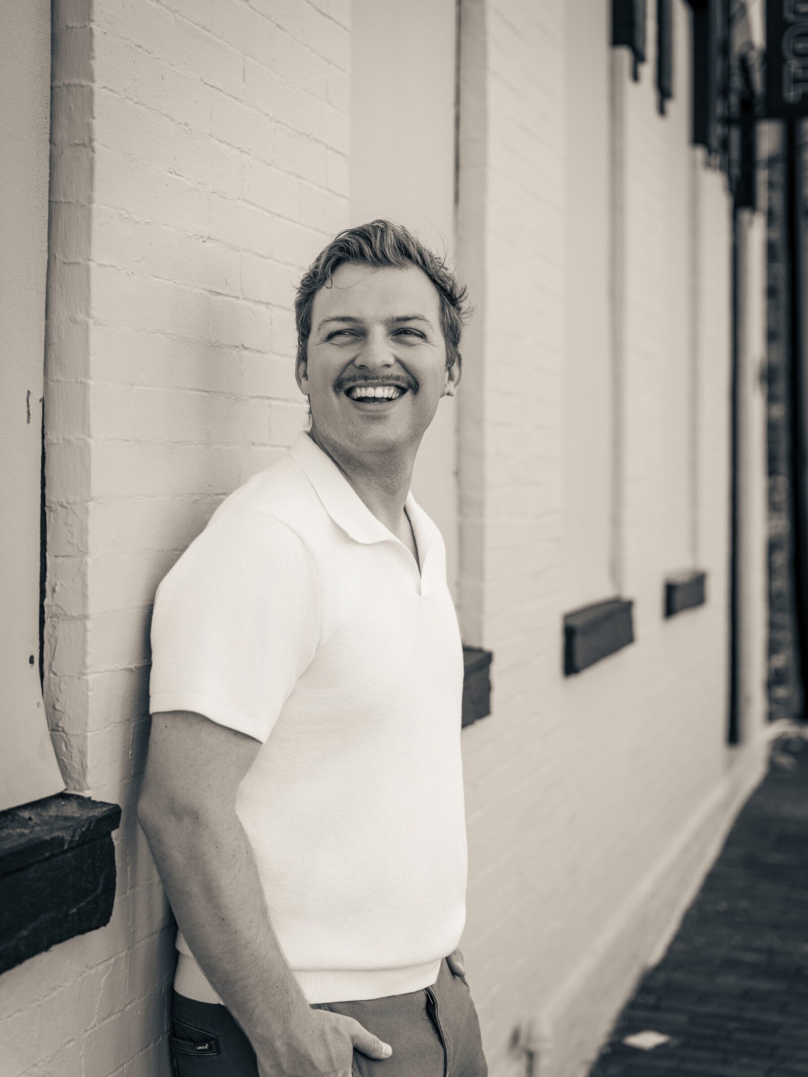 Black-and-white professional portrait of a man smiling beside a brick wall in Washington, D.C.